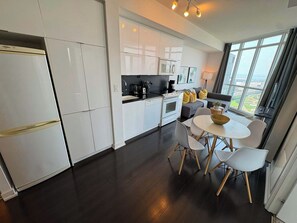A modern kitchen with white cabinets, a dining area with a round table and chairs, and a large window with a view. - Modern Core 1BR Oasis Walk to Rogers Centre! (Toronto)