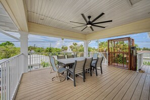 Eine überdachte Terrasse im Freien mit Tisch und Stühlen, einem Deckenventilator und Blick auf die umliegende Landschaft.