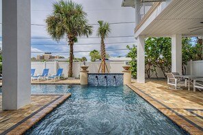 En swimmingpool med et vandfald, omgivet af liggestole og palmer.