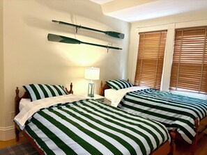 Ein Zimmer mit zwei Betten, einem Nachttisch, einer Lampe und einem Fenster mit Jalousien.