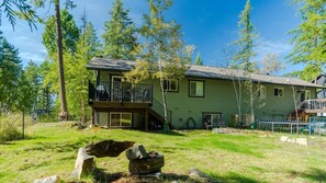 A two-story house with a balcony, surrounded by trees and a grassy yard. - Ridgecrest Lakeview Retreat (Whitefish)