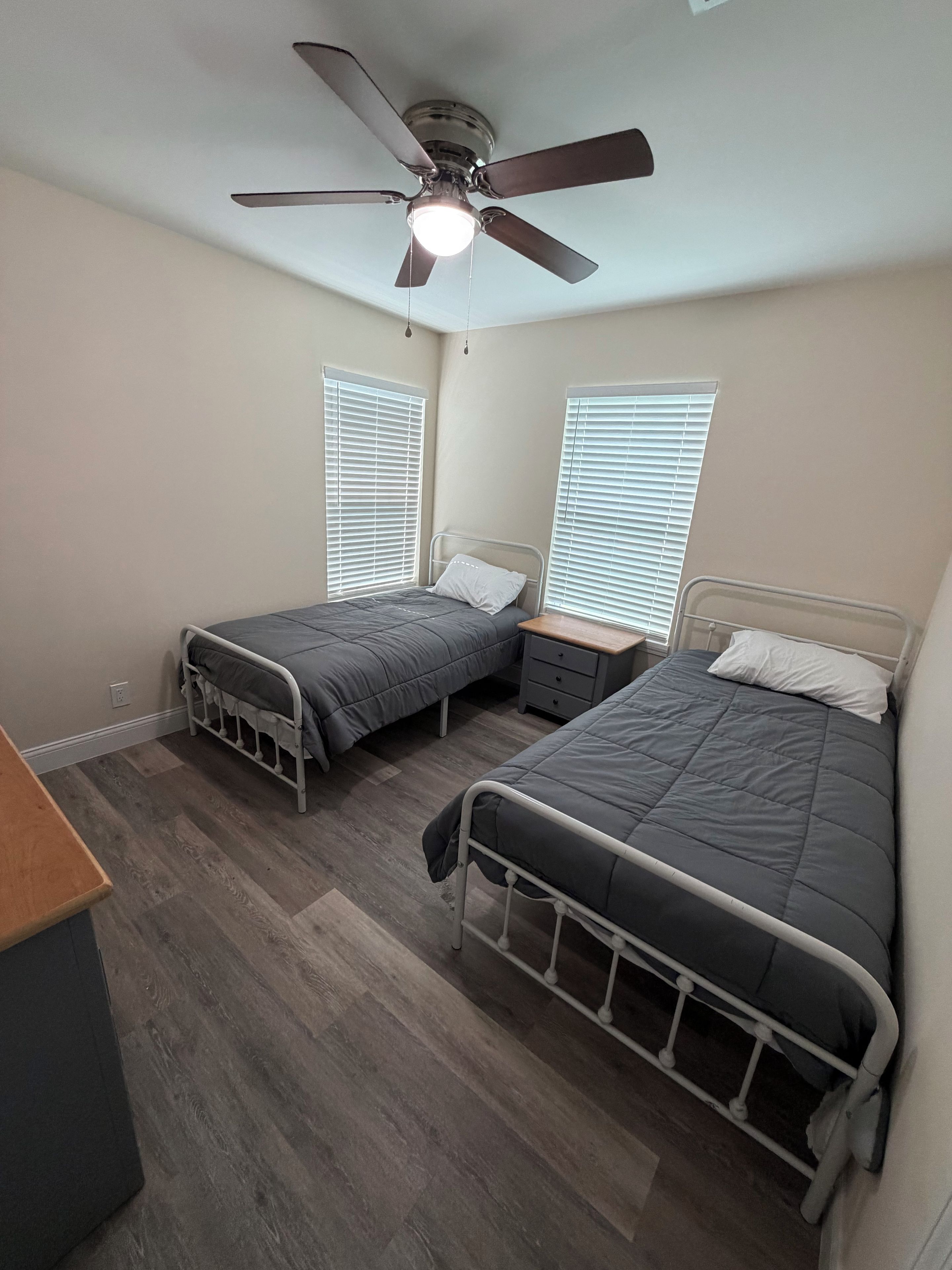 Un dormitorio con dos camas individuales, un ventilador de techo y una ventana con persianas.