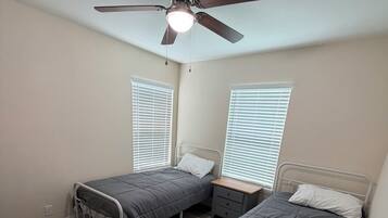 Un dormitorio con dos camas individuales, un ventilador de techo y una ventana con persianas.