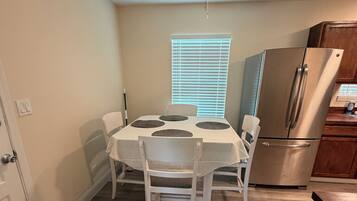 A compact kitchen with a dining table, chairs, a ceiling fan, a refrigerator, and a window with blinds.