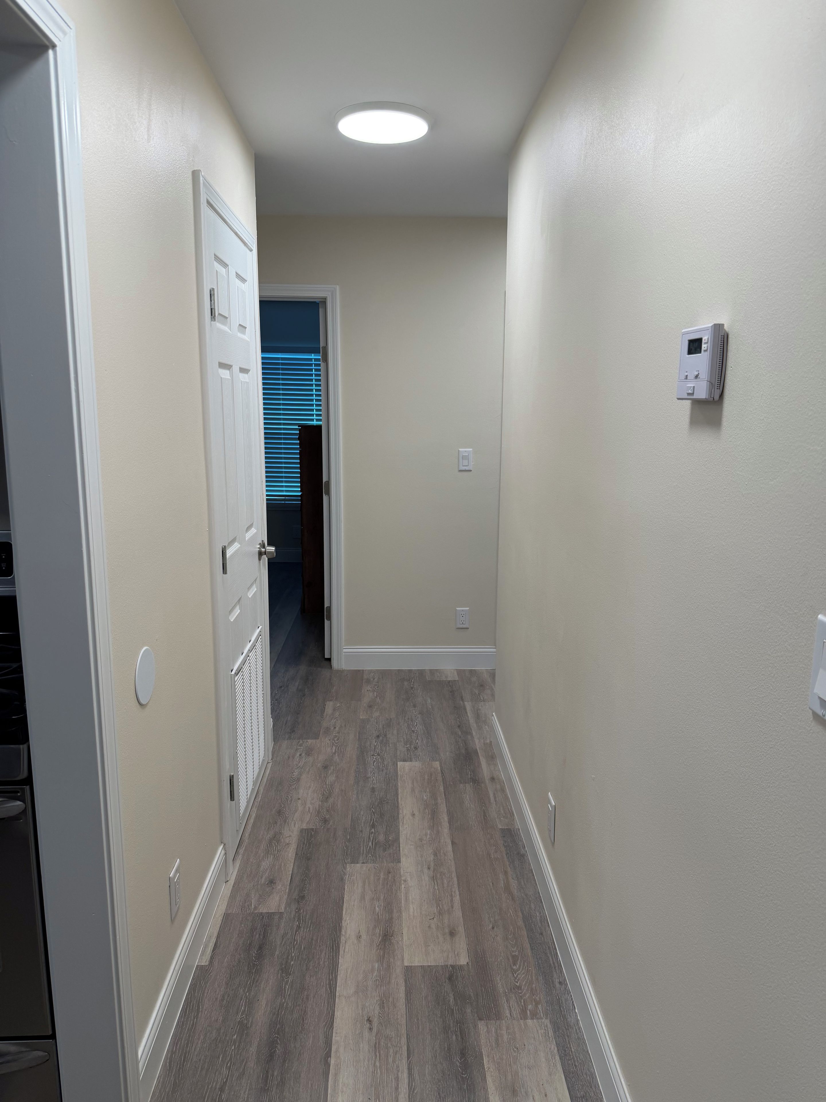 A hallway with a wooden floor, a white door, and a thermostat on the wall.