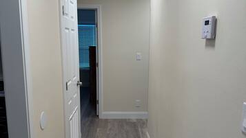 A hallway with a wooden floor, a white door, and a thermostat on the wall.
