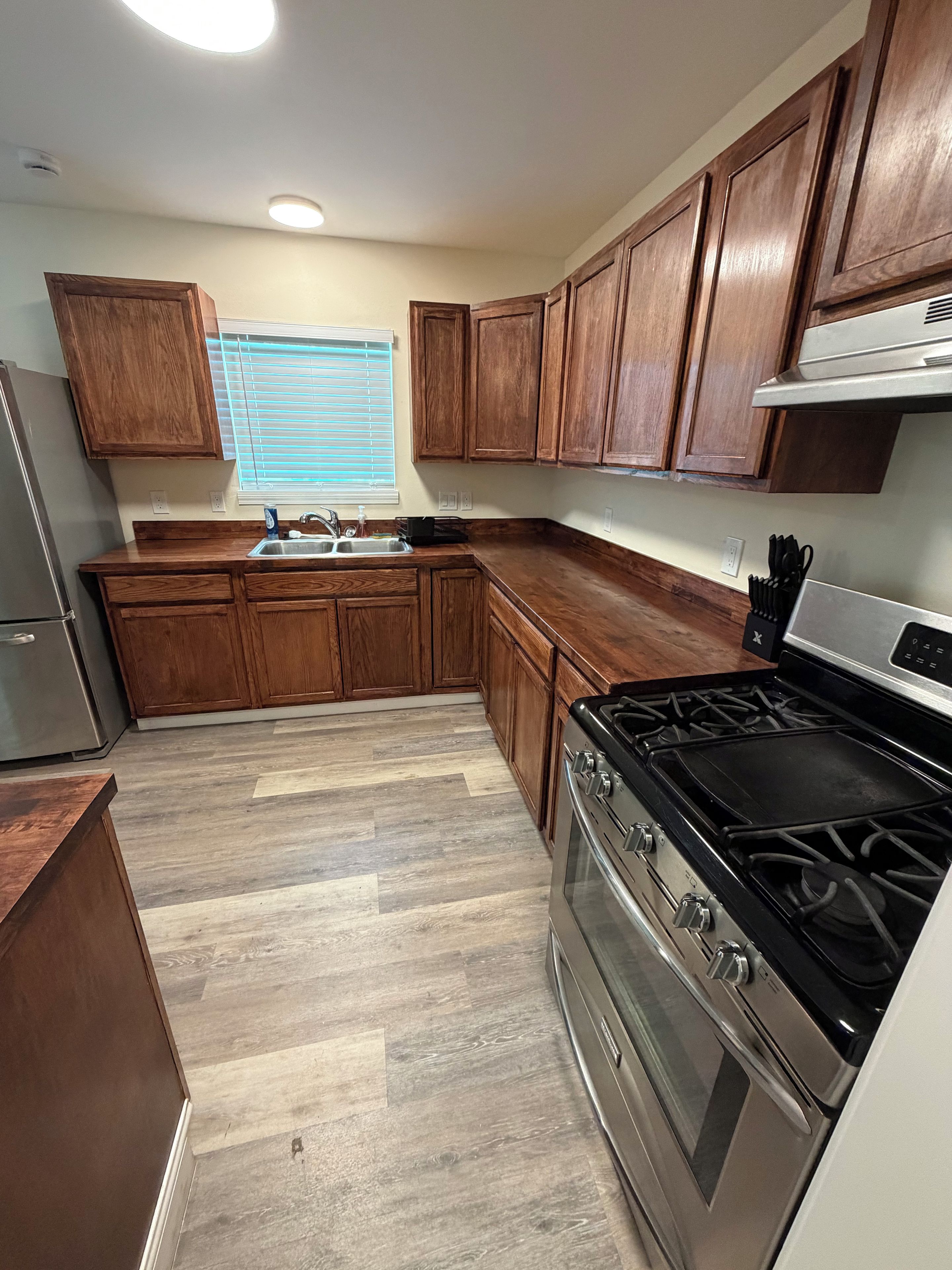 Una cocina con armarios de madera, una estufa de acero inoxidable y una ventana con persianas.