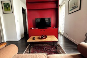 Ett vardagsrum med en röd möbel för underhållningsutrustning, en tv, ett soffbord i trä och en mönstrad matta.