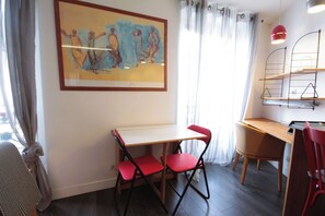 A room with a table, two chairs, a radiator, a painting, and a window with curtains. - Cozy  Flat - La Fayette / Grands Boulevards (Paris)