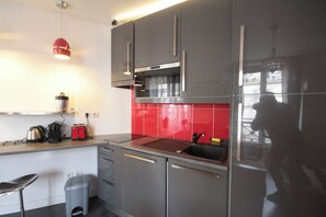 A modern kitchen with stainless steel appliances, a red backsplash, and a hanging pendant light. - Cozy  Flat - La Fayette / Grands Boulevards (Paris)