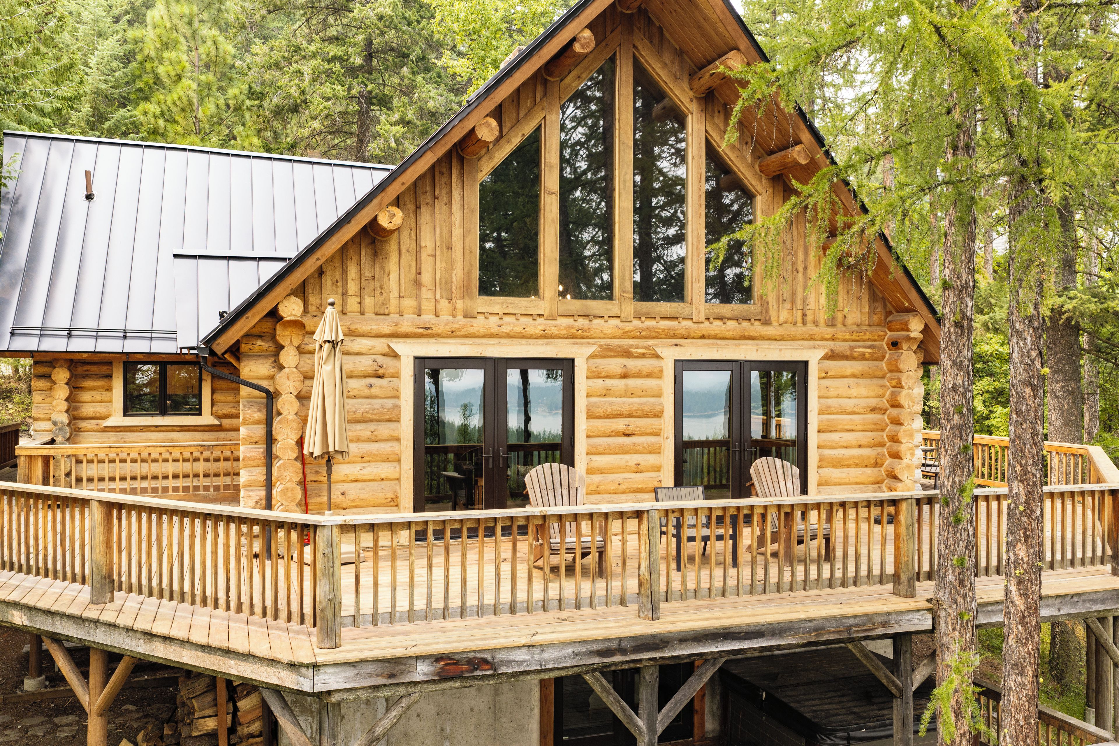 A log cabin with a deck, large windows, and a view of the surrounding forest.