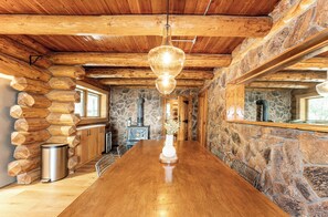 Interior de una cabaña de troncos con una mesa de madera, paredes de piedra y una lámpara colgante.