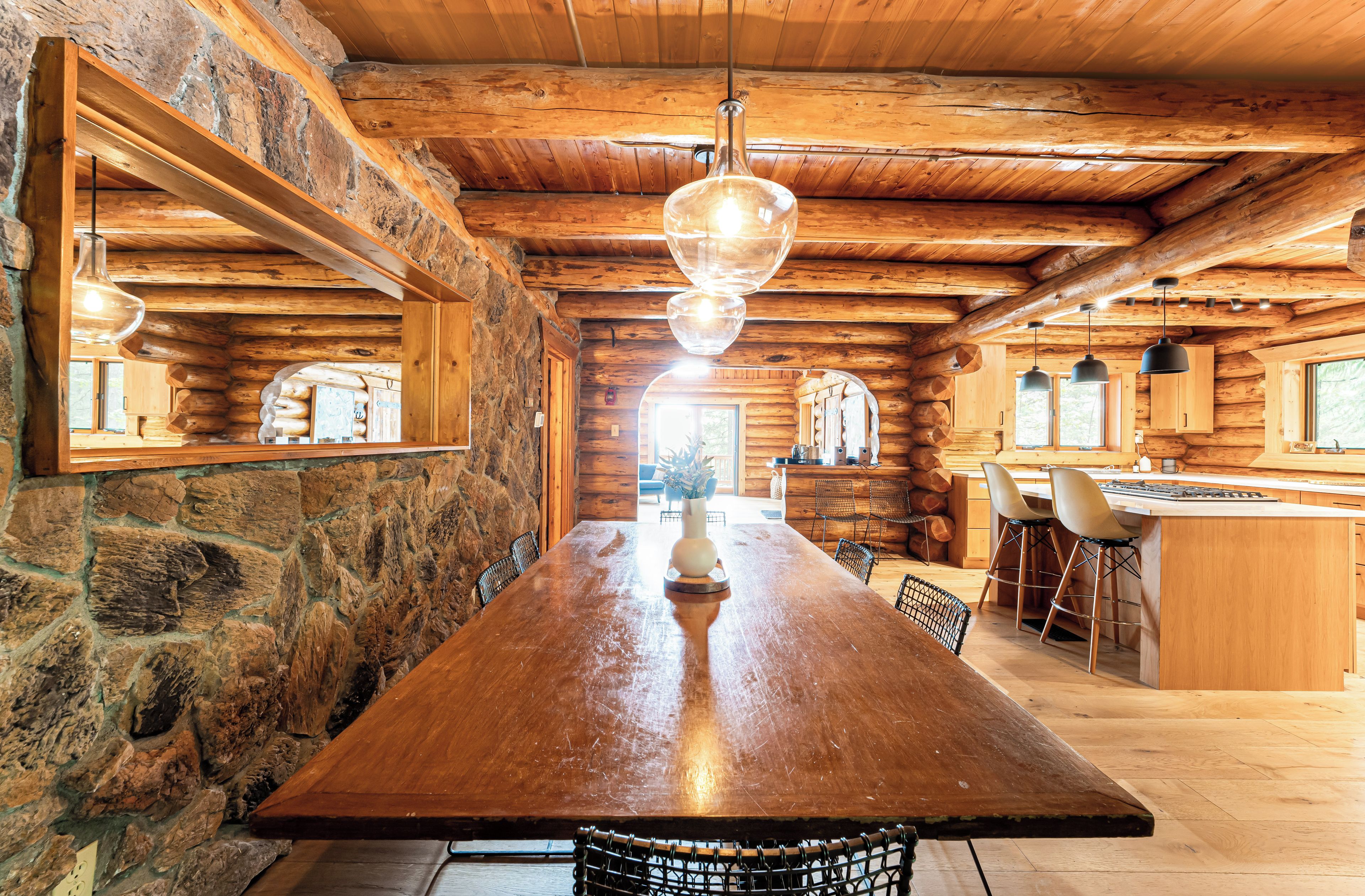 A wooden dining table with chairs, a hanging light fixture, and a stone wall.