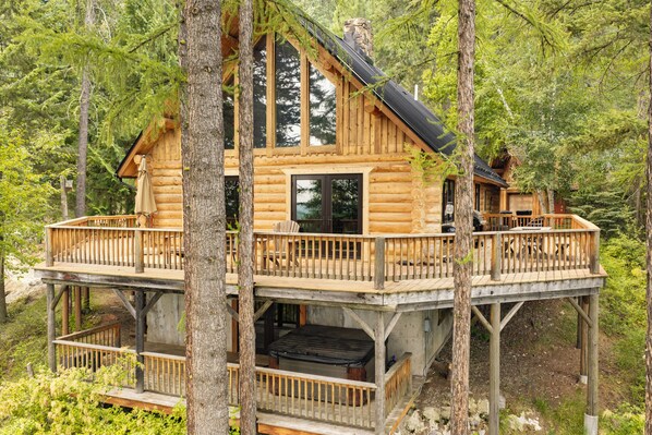 A log cabin with a balcony and deck, surrounded by trees.