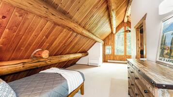 Une pièce avec un plafond en pente, des murs en bois, un lit, une commode et un tableau.