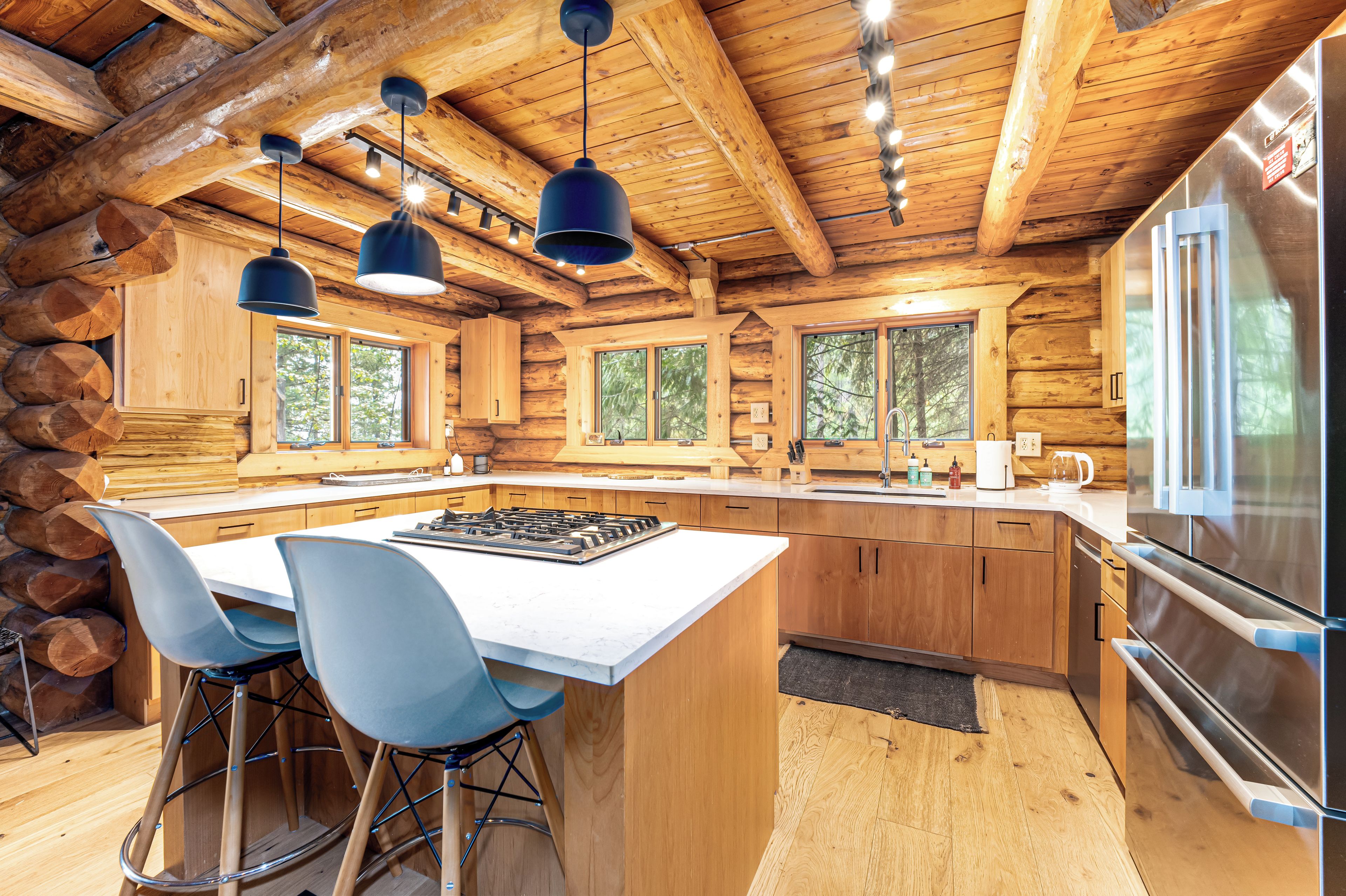A log cabin kitchen with a central island, bar stools, and a large refrigerator.