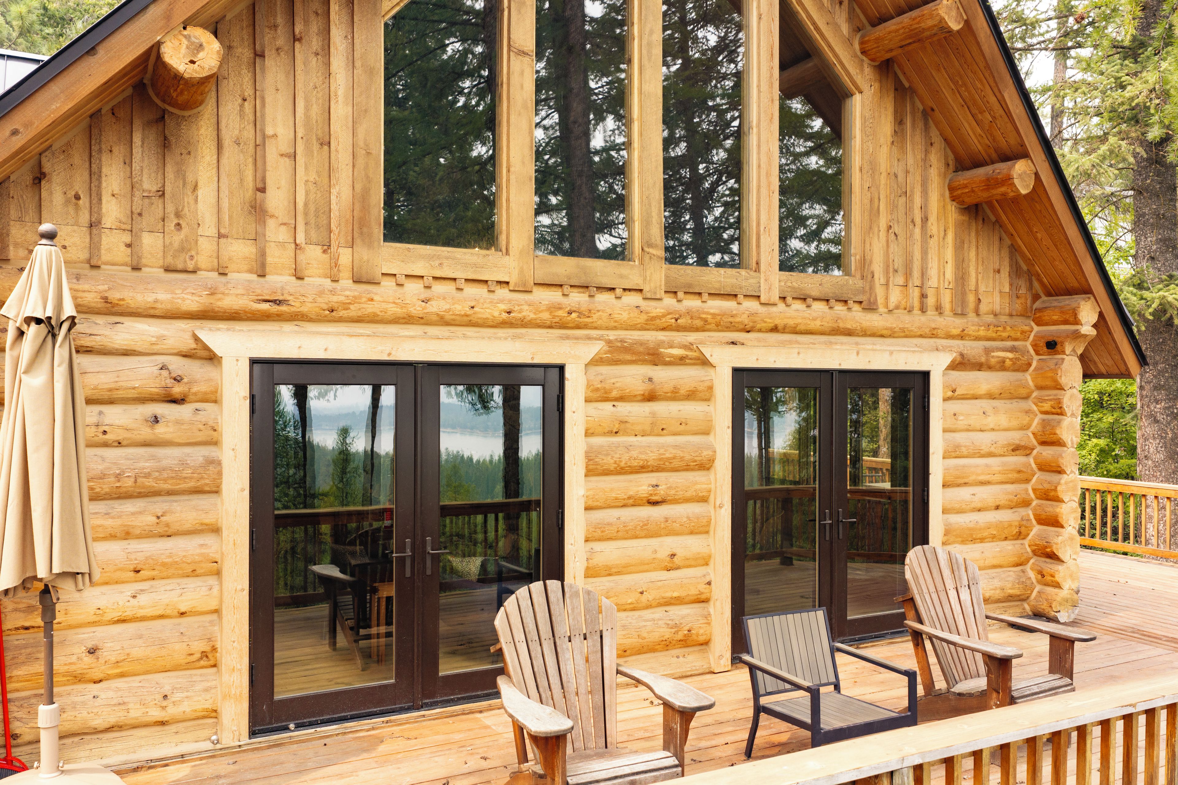 A log cabin with large sliding glass doors, outdoor seating with Adirondack chairs, and a deck overlooking a forested area.