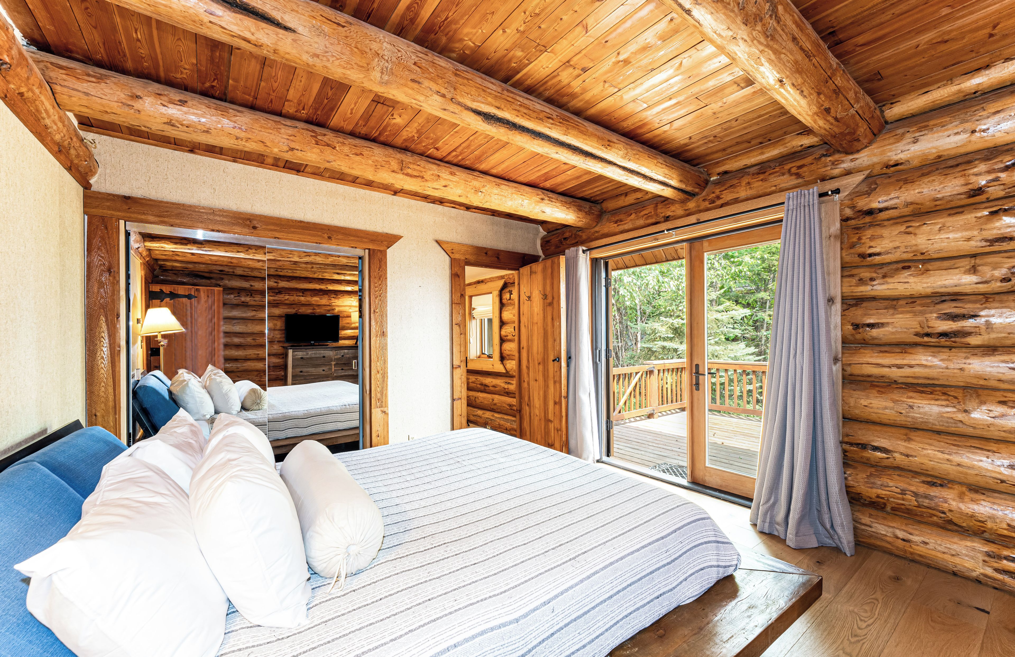Quarto de cabana de madeira com cama, televisão e porta de vidro deslizante para um deck.