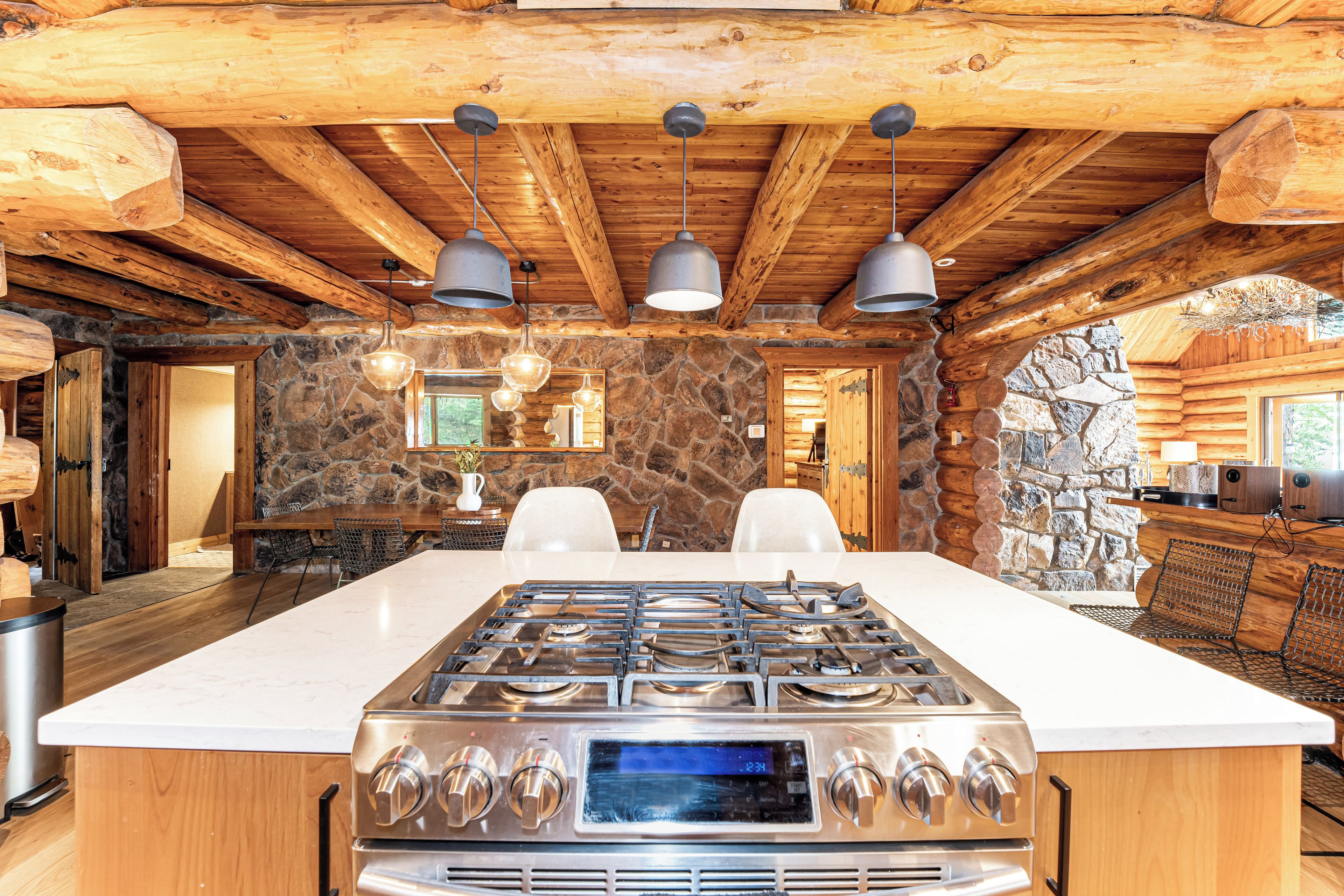 A spacious kitchen with a large island stove, stone walls, and wooden beams.