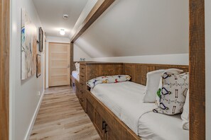 A narrow, single-room hotel bedroom with a wooden headboard, a bed with patterned bedding, and a wooden wardrobe. - Riverfront Retreat | Hot Tub | Fire Pit | Large Groups | Fishing (Gallatin Gateway)