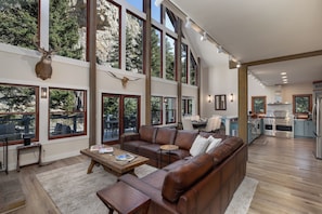 A spacious living room with a brown leather sofa, a wooden coffee table, and a dining area with a table and chairs. - Riverfront Retreat | Hot Tub | Fire Pit | Large Groups | Fishing (Gallatin Gateway)