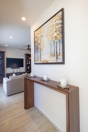 Uma sala de estar moderna com mesa consola de madeira, uma pintura grande, televisão de tela plana e um sofá.