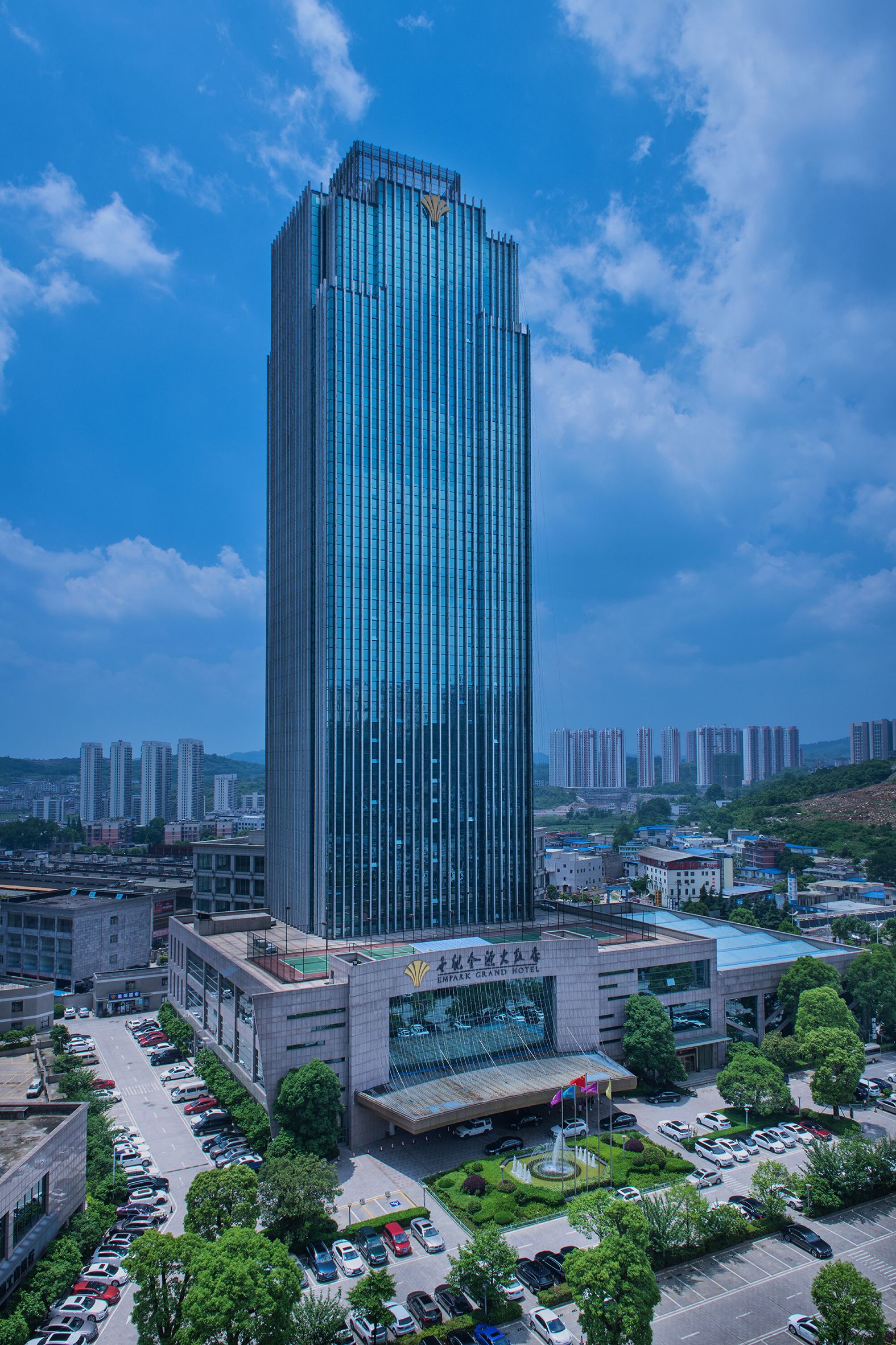 Un hôtel moderne de grande hauteur, caractérisé par une architecture verticale imposante, un parking et des bâtiments urbains environnants.