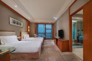Habitación de hotel con dos camas, televisión, escritorio y baño visible a través de una puerta abierta.
