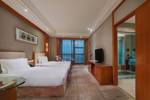 A hotel room with two beds, a television, a desk, and a bathroom visible through an open door.