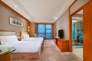 Ein Hotelzimmer mit einem großen Bett, einem Fernseher, einem Schreibtisch und Meerblick durch das Fenster.