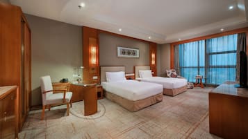 A hotel room with two beds, a desk, a chair, a television, and a large window with curtains.