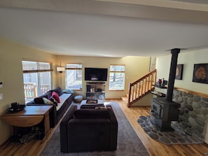 A living room with a sofa, ottoman, TV, fireplace, and a staircase. - Charming 3-bedroom house in serene Bend with woodsy comfort (Bend)