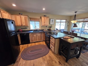 A kitchen with wooden cabinets, a black refrigerator, a stove, and a dining area with a table and chairs. - Charming 3-bedroom house in serene Bend with woodsy comfort (Bend)