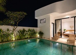 A modern outdoor pool area with a clear pool, two lounge chairs, and a well-lit interior bedroom visible through glass doors. - Bohemian Chic Villa Brand New 2BR with Private Pool, Next To Obsidian & Paddle (Kabupaten Badung)