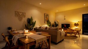 A living room with a sofa, a TV, a dining table with candles, and a lamp. - Bohemian Chic Villa Brand New 2BR with Private Pool, Next To Obsidian & Paddle (Kabupaten Badung)