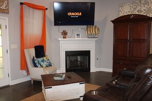 A living room with a fireplace, a television mounted above it, a leather sofa, and a coffee table with books. - Spacious 5-bedroom house in lovely Oxford with AC comfort (Oxford)