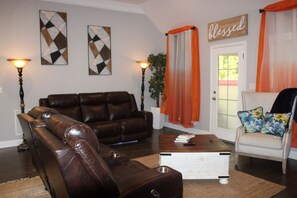 A living room with a brown leather sofa, a white coffee table, and orange curtains. - Spacious 5-bedroom house in lovely Oxford with AC comfort (Oxford)