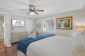 Ein Schlafzimmer mit einem Bett, einem Deckenventilator, einem Fenster mit Jalousien, einer Tür, einem gerahmten Bild und einem Schild für Anna Maria Rental Properties.