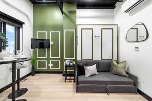 Ein modernes Wohnzimmer mit einem grauen Sofa, einem kleinen Tisch mit einer Vase und einer Schale, einem flachbildfernseher an der Wand und einer grünen Wand mit weißem Zierleiste.
