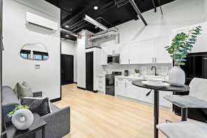 A modern kitchen with white cabinets, a black stove, and a dining area with a round table. - Experience Downtown Energy Near Petco Park & Dine! (San Diego)