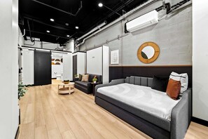 Ein modernes Schlafzimmer mit einem grauen Sofa, einem runden Spiegel und einem Holzboden.