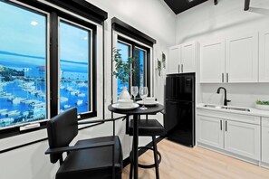 A modern kitchen with white cabinets, a black refrigerator, and a dining area with a table and chairs. - Feel Downtown Energy Near Petco Park & Top Dining! (San Diego)