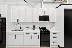 A modern kitchen with white cabinetry, a stainless steel range, a built-in microwave, and a black refrigerator. - Feel Downtown Energy Near Petco Park & Top Dining! (San Diego)