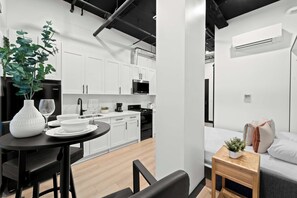 A modern kitchen with white cabinets, a black stove, and a dining area with a table and chairs. - Feel Downtown Energy Near Petco Park & Top Dining! (San Diego)
