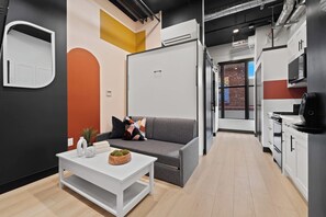 A modern interior with a grey sofa, white coffee table, and a kitchen area with a stove and cabinets. - Live Downtown Steps From Petco Park & Gaslamp Fun! (San Diego)