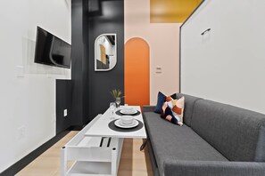 A modern living space with a dining area, a grey sofa, and a TV mounted on the wall. - Live Downtown Steps From Petco Park & Gaslamp Fun! (San Diego)