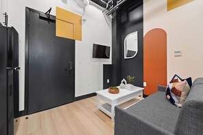 A modern living space with a black door, a white table with decorative items, a grey sofa, and a wall-mounted mirror. - Live Downtown Steps From Petco Park & Gaslamp Fun! (San Diego)