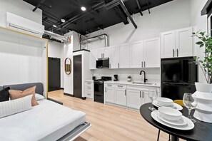 A modern kitchen with white cabinets, a black refrigerator, and a dining area with a table set for two. - Discover Downtown Nights Near Petco Park & Dining! (San Diego)