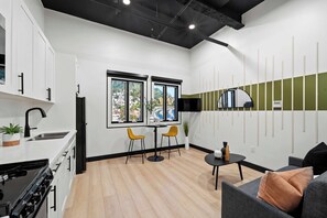 A modern kitchen with white cabinets, a black stove, and a dining area with two yellow chairs and a table. - Discover Downtown Nights Near Petco Park & Dining! (San Diego)