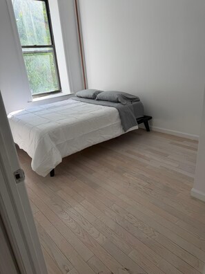 A bedroom with a bed, a window, and a wooden floor. - Extra large 4 bedroom 2 bathroom in Manhattan- full kitchen, dining table + more (New York)